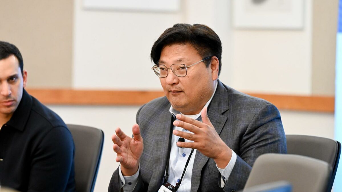 A man in a suit jacket gestures with his hands.