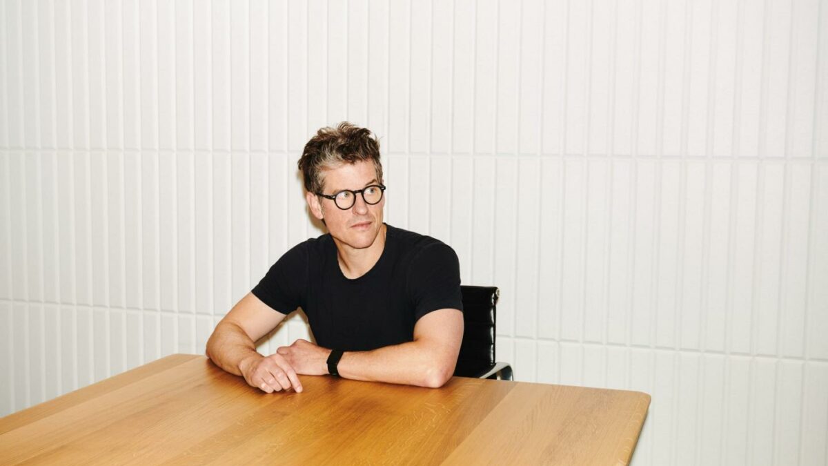 Fragment CEO sitting down with arms resting on a wooden table as he looks to his left.