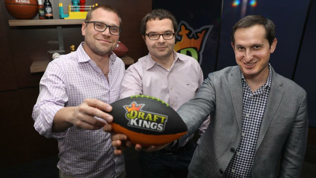 Matthew Kalish (left), Paul Liberman (middle), and Jason Robins (right), hold up a football with the DraftKings logo printed on it.