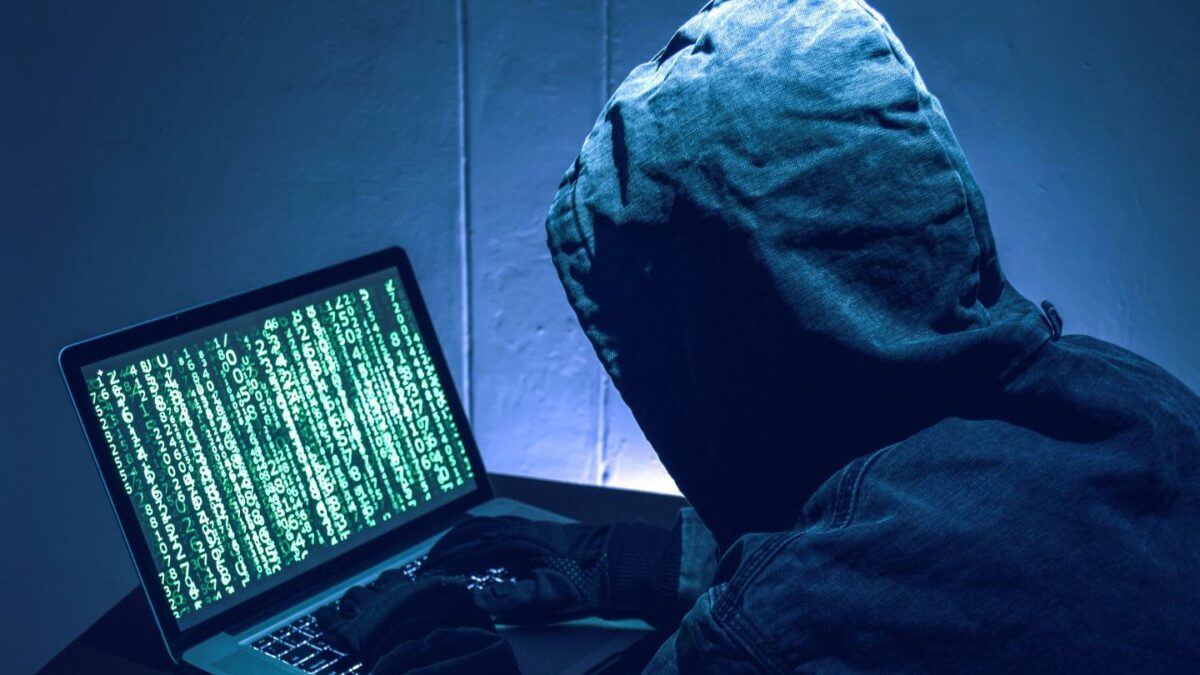 A hacker wearing a hoodie sitting at a laptop.