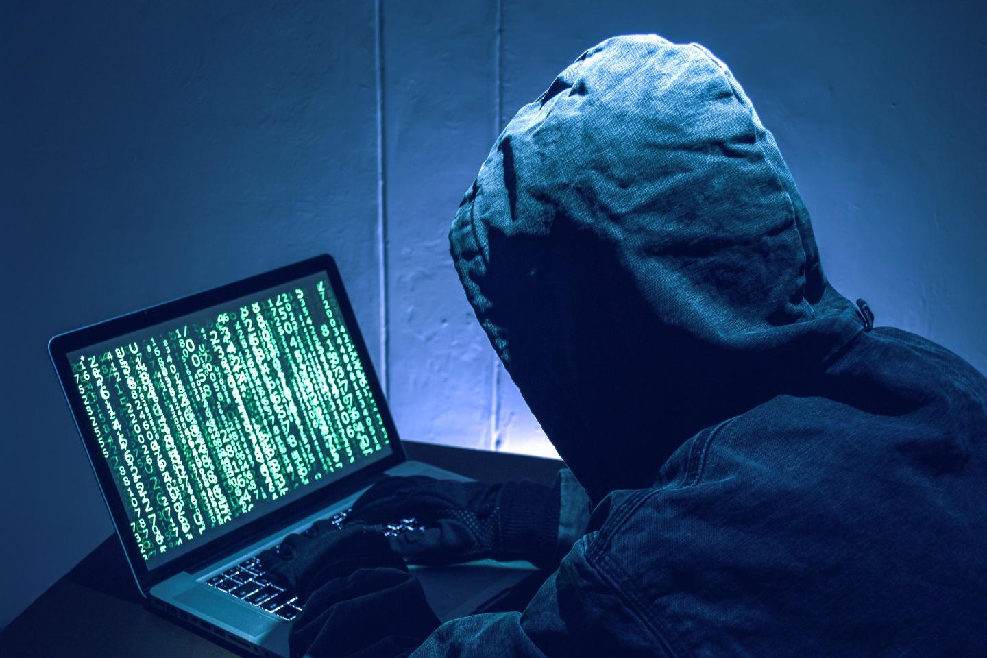 A hacker wearing a hoodie sitting at a laptop.