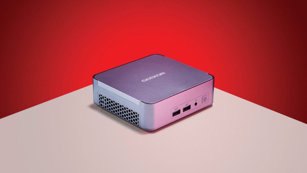 A Geekom Mini PC sitting on a white table against a red background.