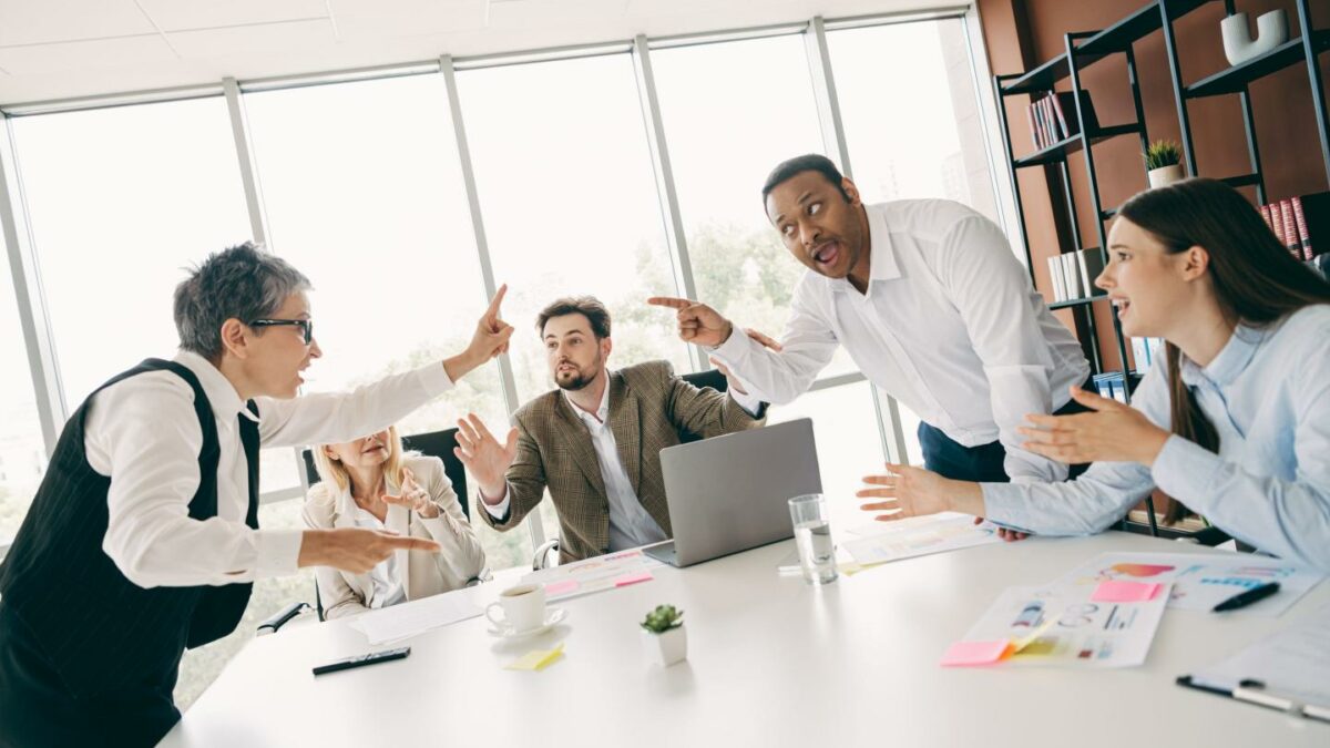 People pointing at each other in a boardroom.