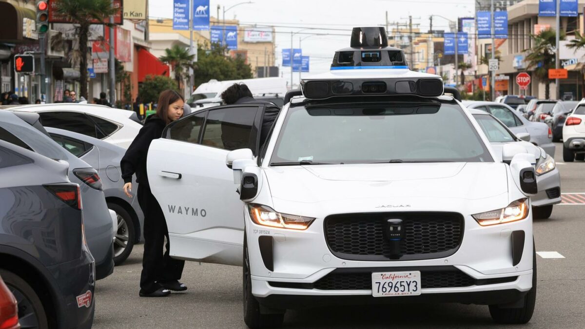 A woman gets out of a white Waymo van.