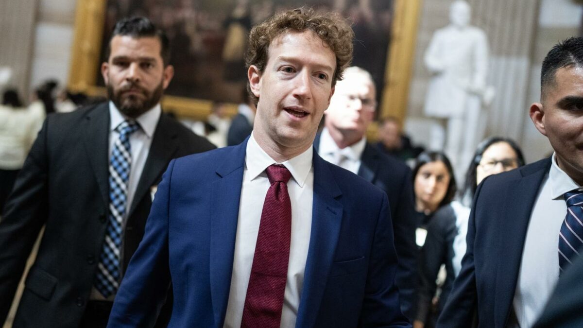 Mark Zuckerberg wears a blue suit, white shirt, and red tie