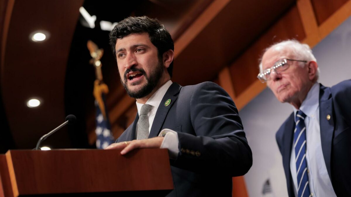 Photo of Rep. Greg Casar at the podium with Sen. Bernie Sanders in the background