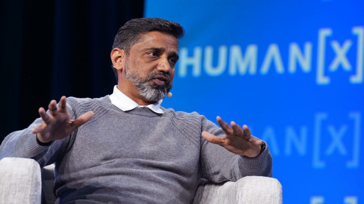 Praveen Neppalli Naga sits in a white chair in front of a blue background onstage.