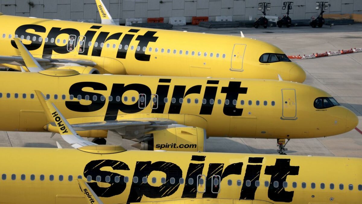 Three Spirit Airlines jets, painted in the company's yellow and black livery, lined up on an airport tarmac.