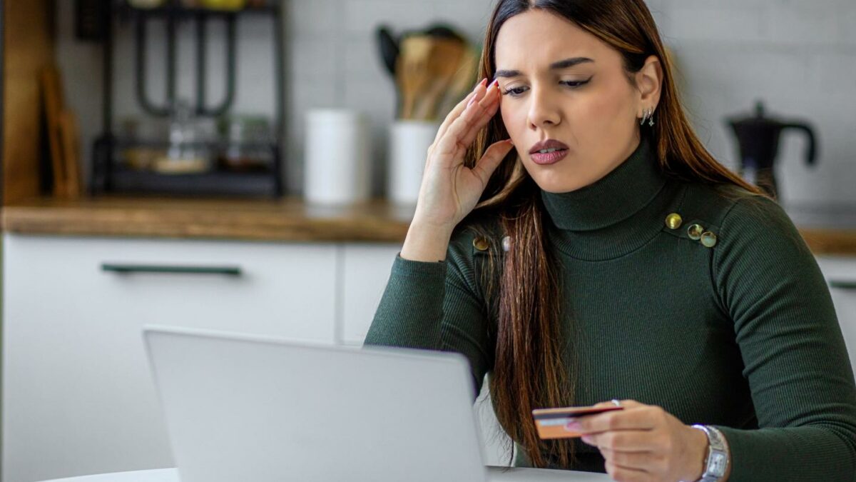 Concerned young woman holding credit card while using laptop