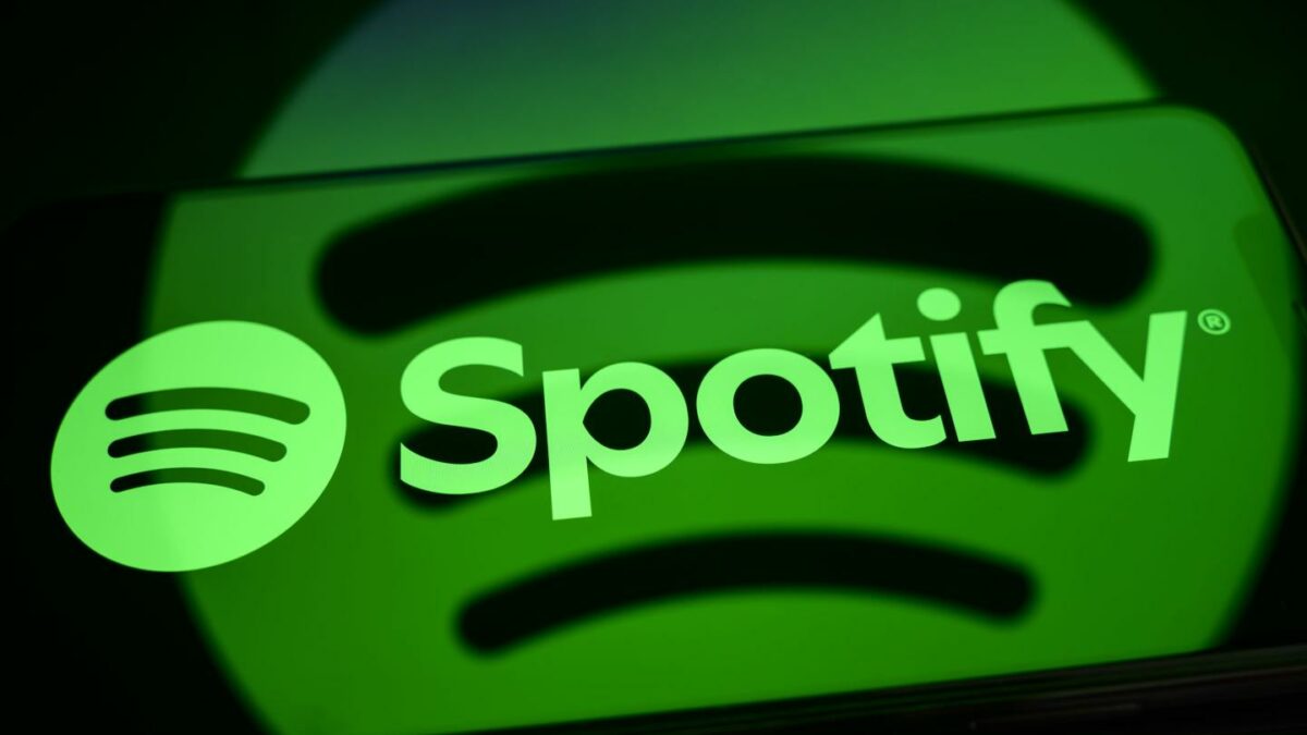 The Spotify logo is displayed on a smartphone screen placed on a reflective surface onto which the company's logo is projected.