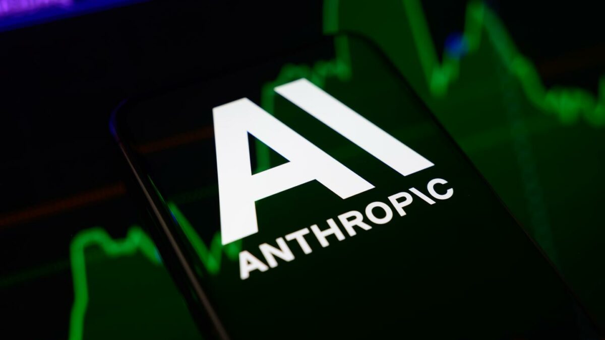 The Anthropic logo is displayed on a smartphone screen placed on a reflective surface onto which a stock market chart is projected.
