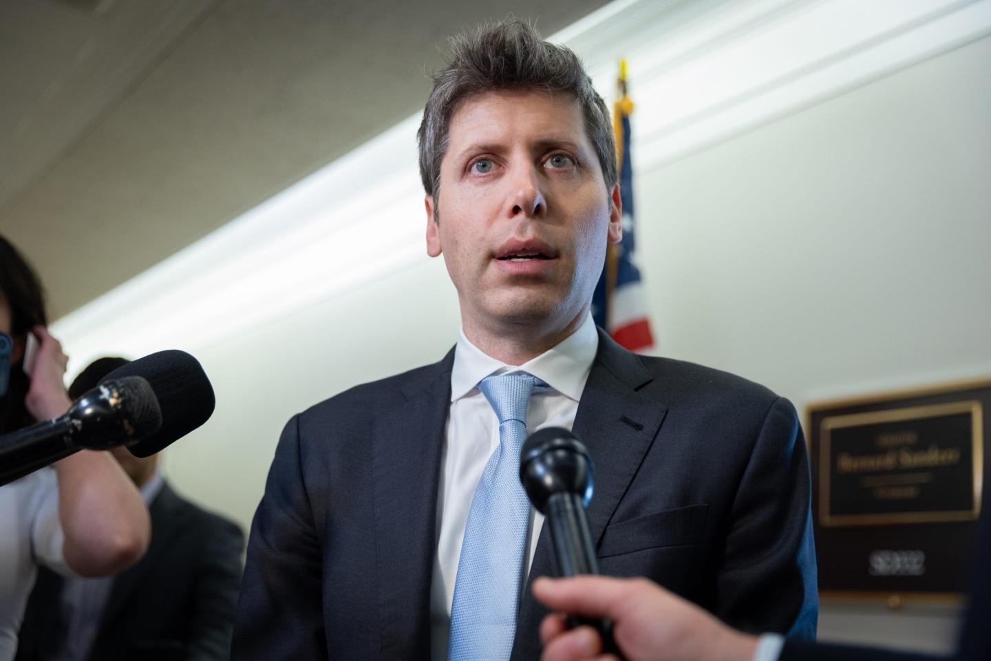 gettyimages-2278967313-e1786657208430-1 Sam Altman stands in front of microphones in a suit