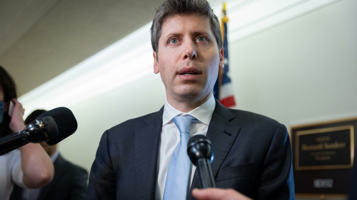 Sam Altman stands in front of microphones in a suit