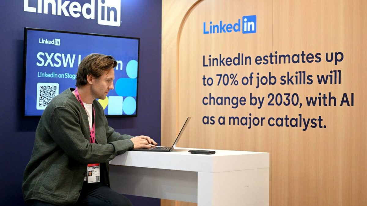 A man sits at a desk with a LinkedIn display behind him.
