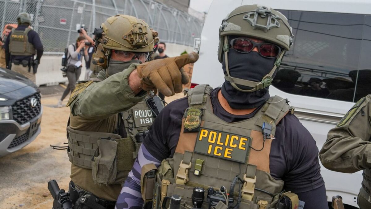 Two ICE agents wearing camouflage gear with eye and face coverings.
