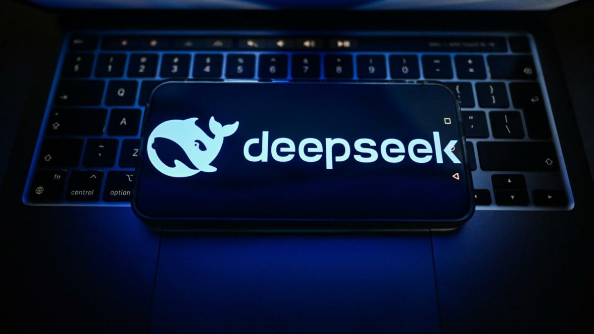 A DeepSeek logo is seen displayed on a smartphone on the top of a laptop.