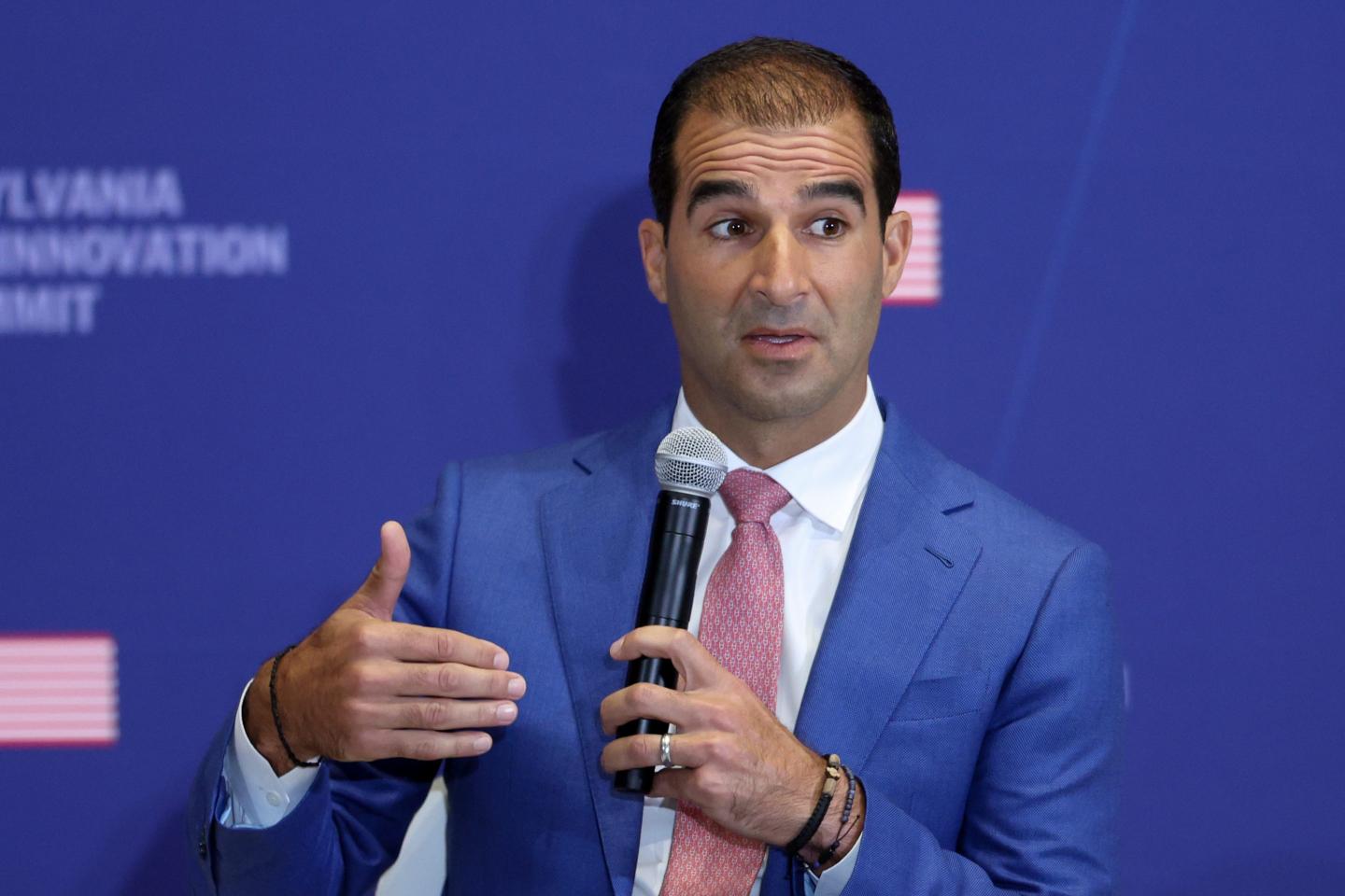 Dino Mavrookas wearing a blue suit and holding a microphone