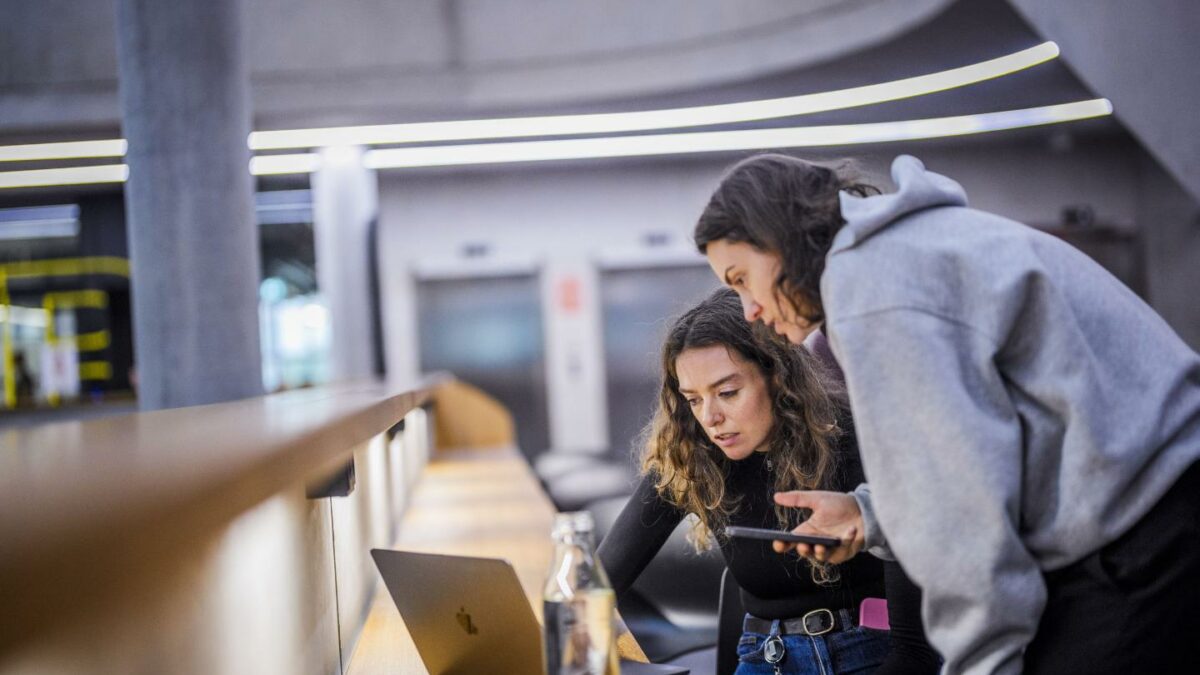 Photo of two young women hunching over laptop
