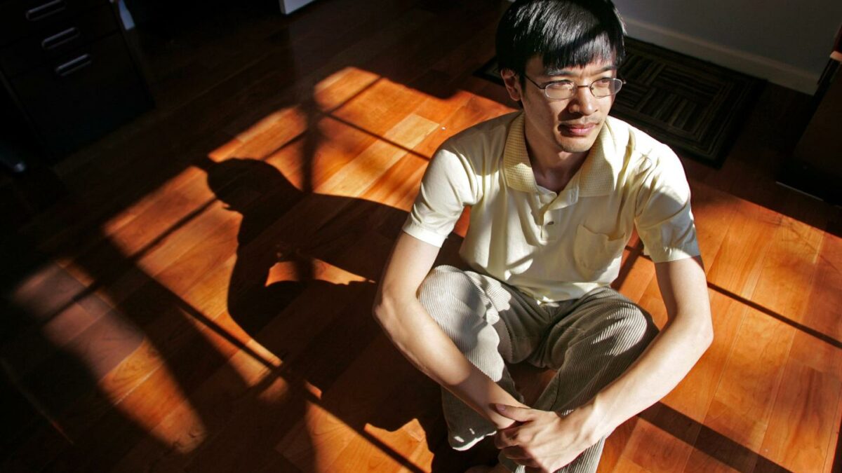 Photo of mathematician Terence Tao sitting cross-legged on a wood floor, partly in sun and partly in shadow, shot from above.