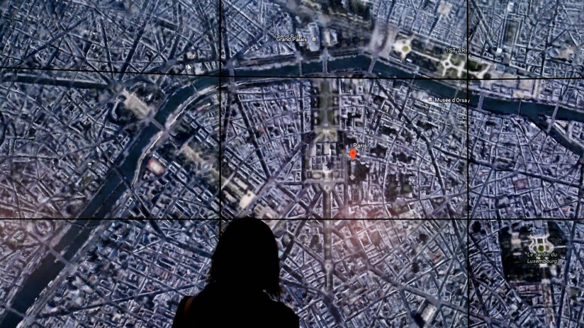 People look at a Google Earth map of Paris,France on a screen as Google Earth.