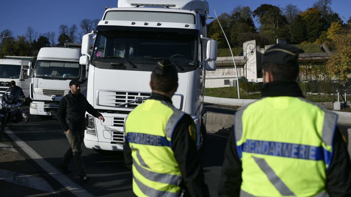 Two people in yellow safety vests look at a while trailer truck.