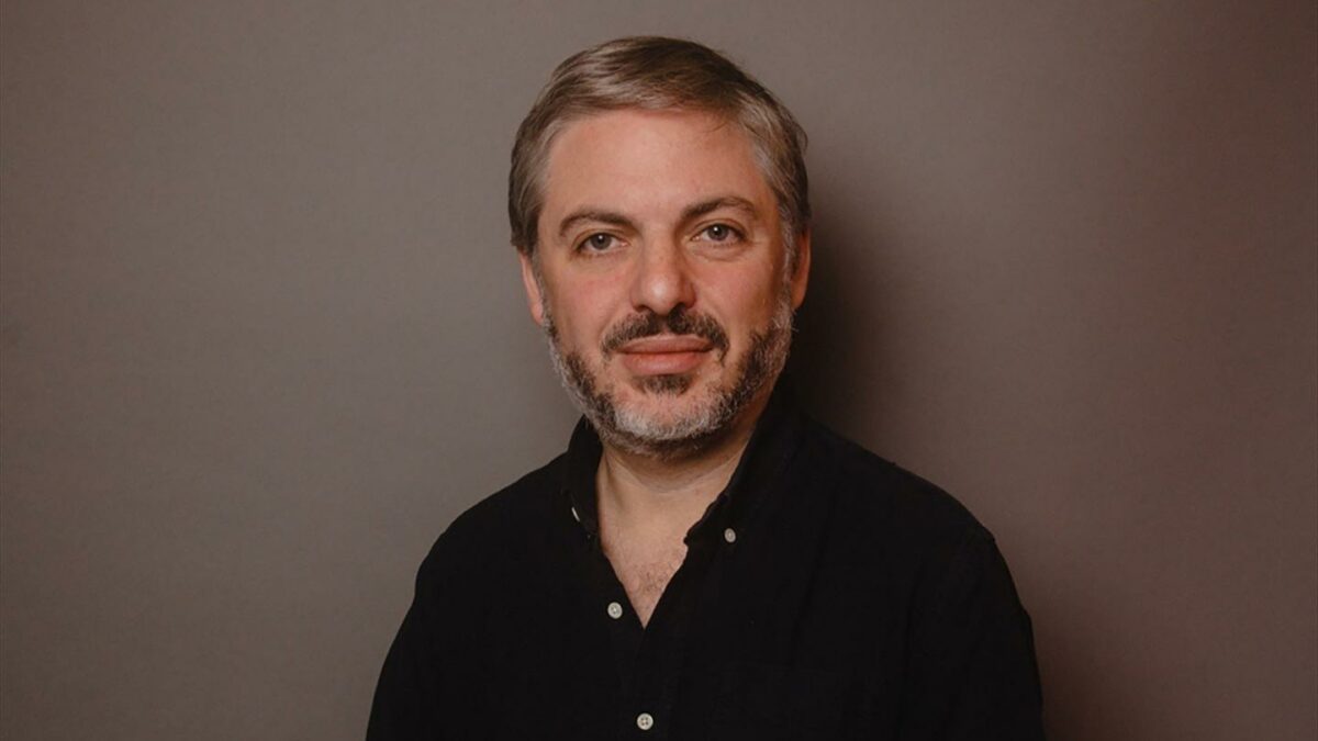 Daniel Simon smiles for a headshot wearing a black button up.