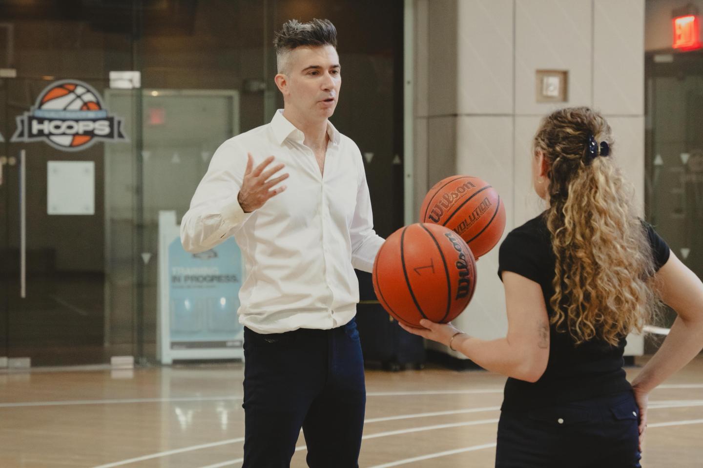 photo-2026-05-26-20-11-50-4-1 Yevgeny Dibrov speaks with a basketball in his hand to a blonde woman also holding a basketball